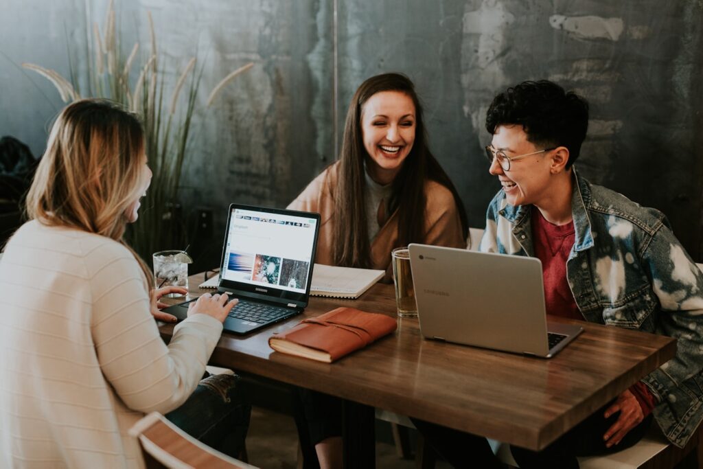 3 Personen sitzen lächelnd am Laptop während eines Beratungsgesprächs (KI-generiertes Symbolbild)