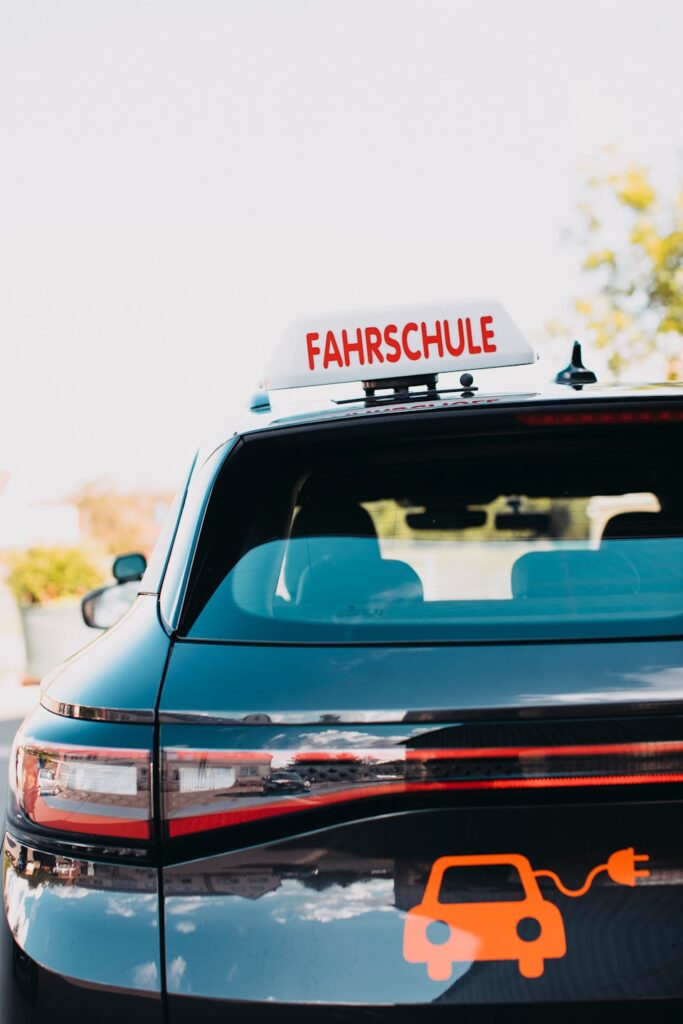 Heckansicht eines Fahrschulautos mit Dachschild Fahrschule und Elektroauto-Ladesymbol (KI-generiertes Symbolbild)
